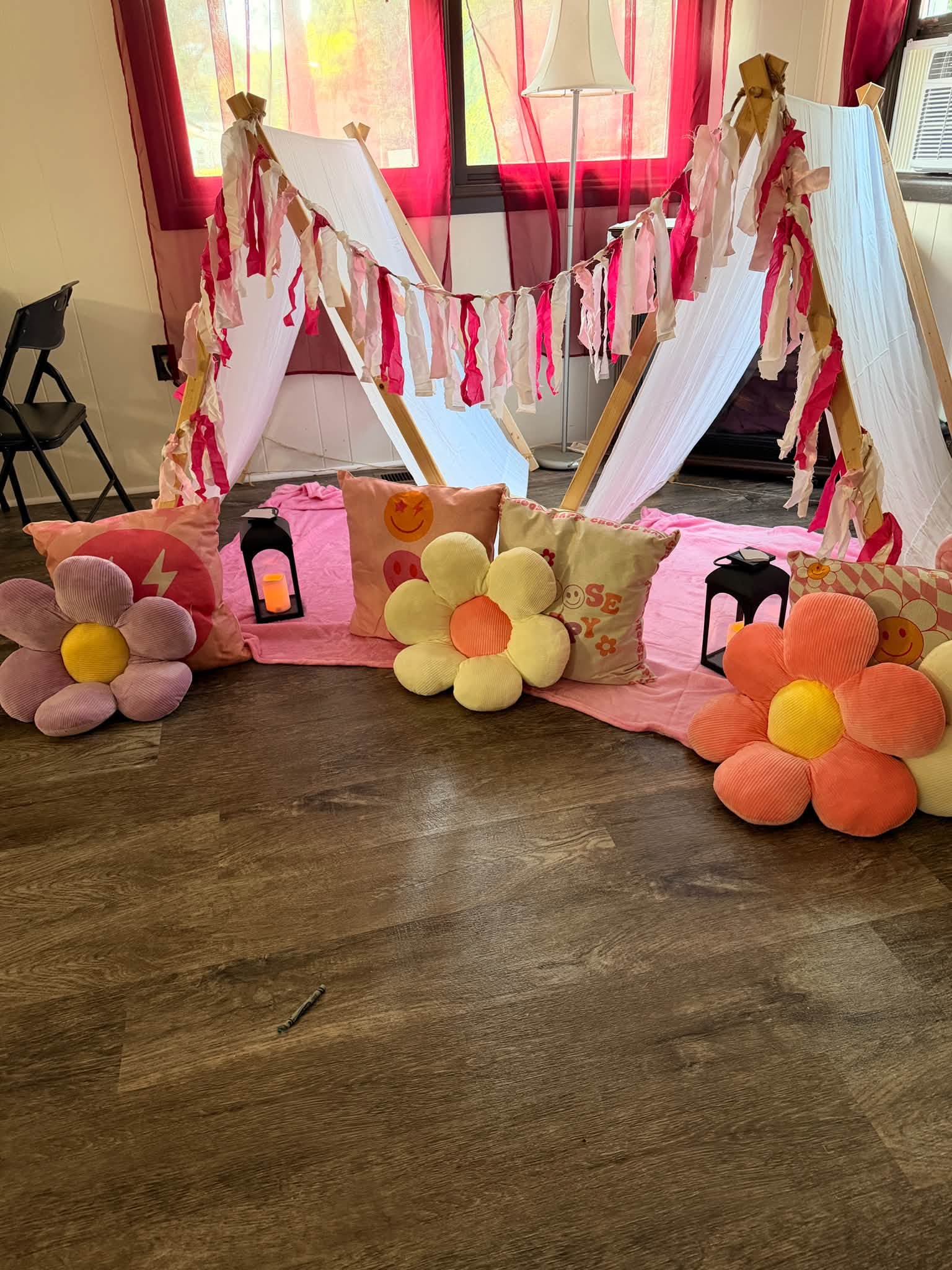 Two teepee tents styled with pink tassel garland and flower pillows as a celebration backdrop