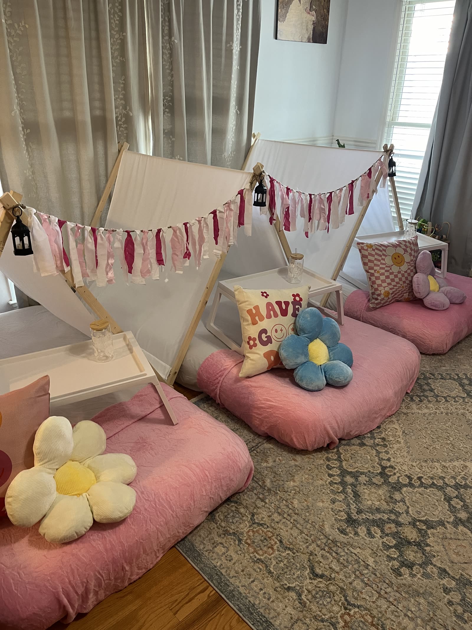 Three pink teepee beds by a window with daisy pillows and bed trays